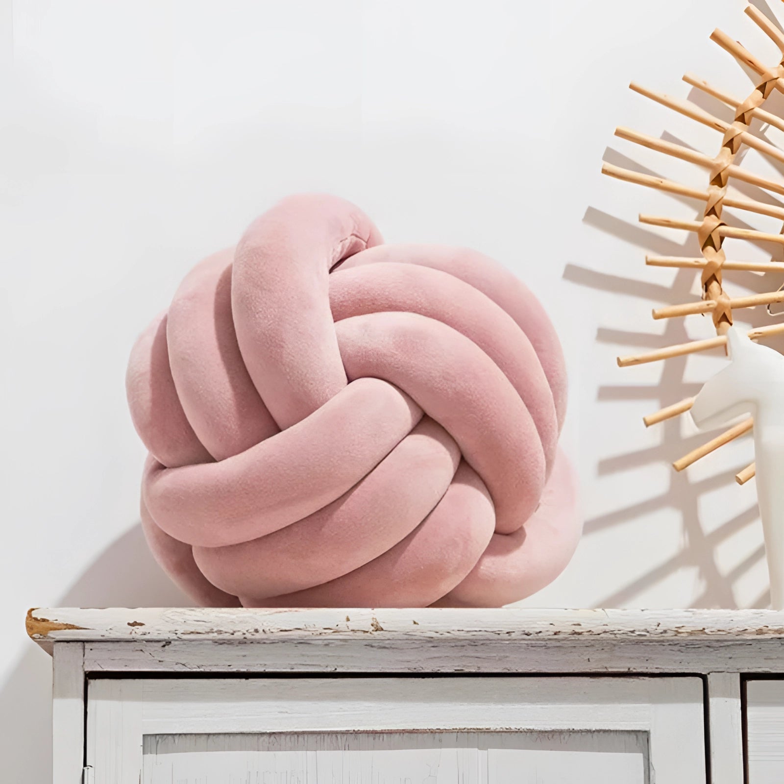 Scandinavian Knot Pillow in pink velvet with a modern decorative design, placed on a wooden surface near a window.