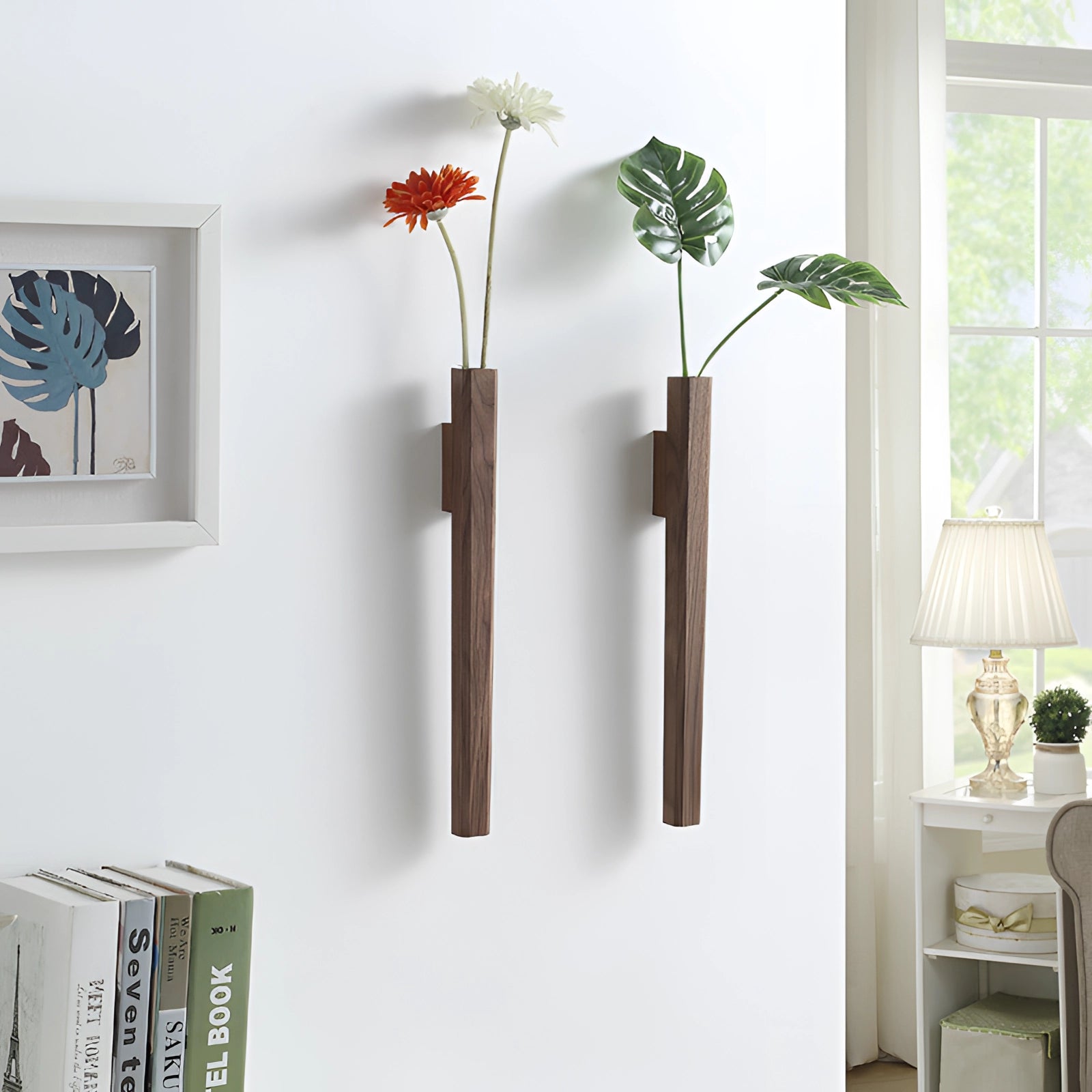 Wooden wall-mounted Scandinavian flower vase with a minimalist design, featuring a vertical holder displaying a flowering plant against a background that includes a window and wooden elements.