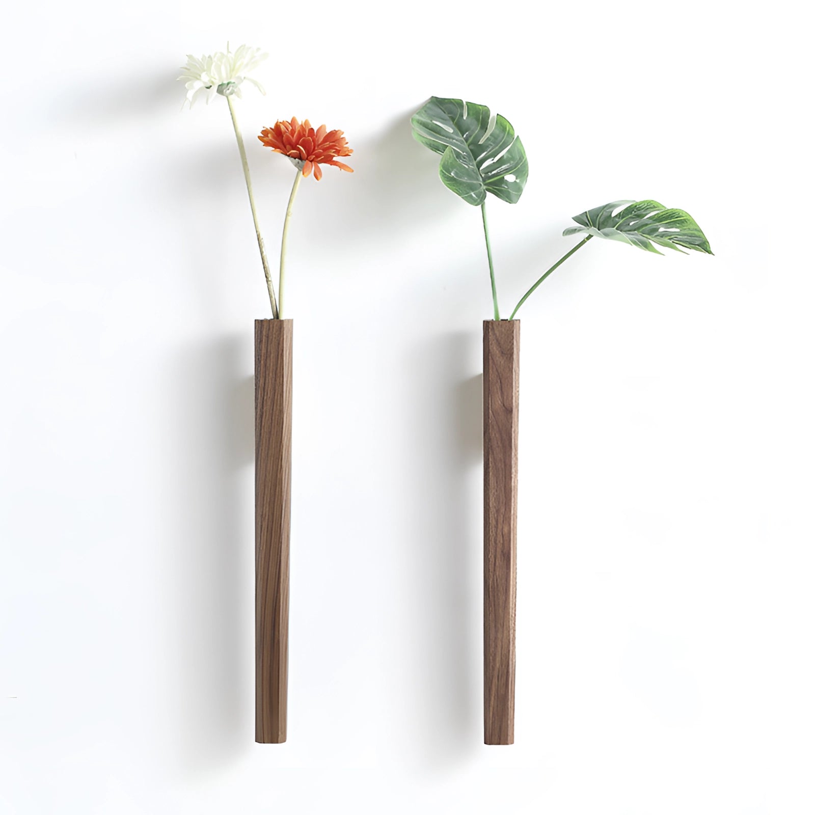 Scandinavian wall-mounted wooden flower vase in black walnut, featuring a minimalist vertical design with a single artificial flower arrangement and twigs, showcasing a natural and stylish decor element.