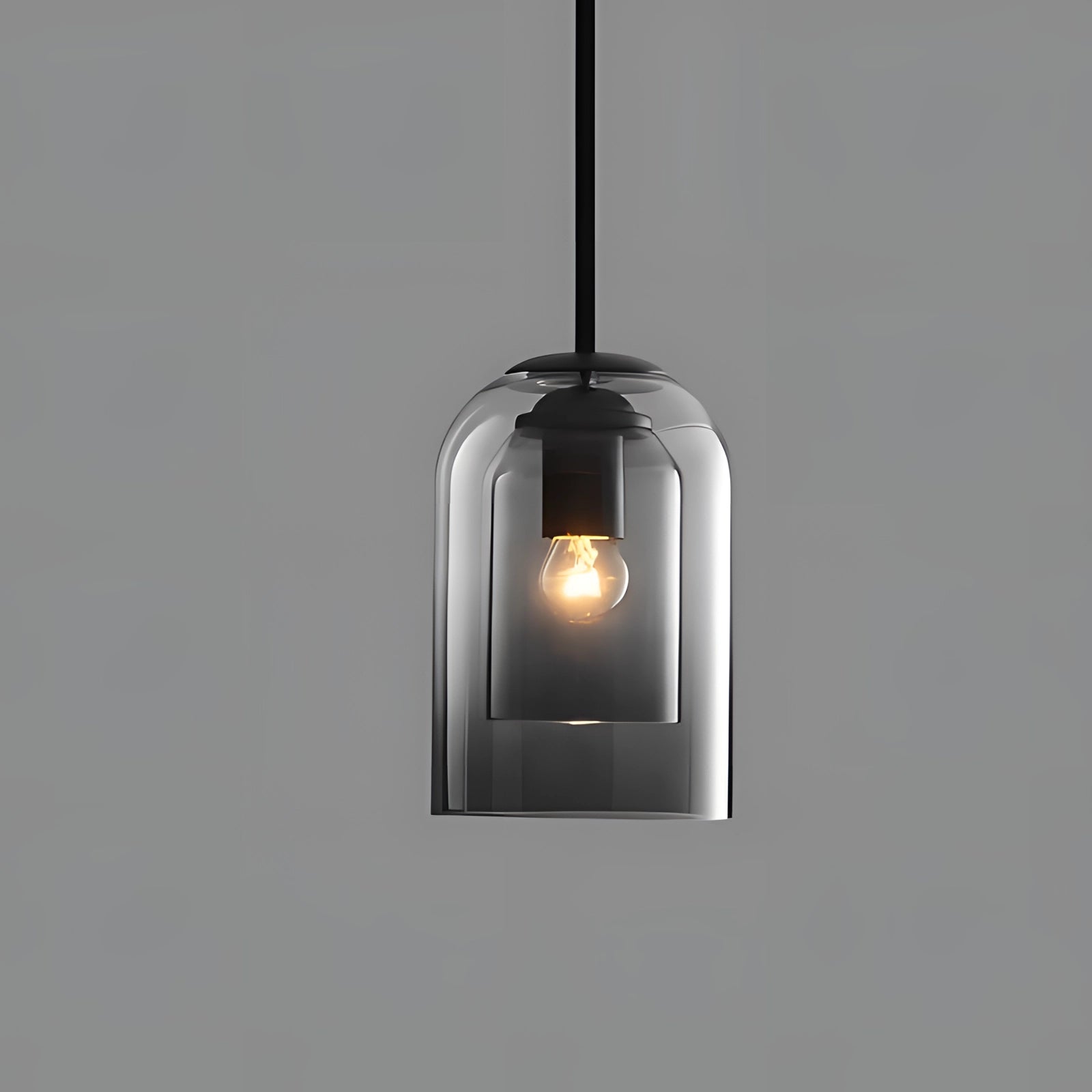 Smoke gray glass pendant light featuring a modern design with a transparent shade, showcasing a visible Edison bulb. The light hangs from the ceiling, with metal and wood elements adding to its contemporary aesthetic.