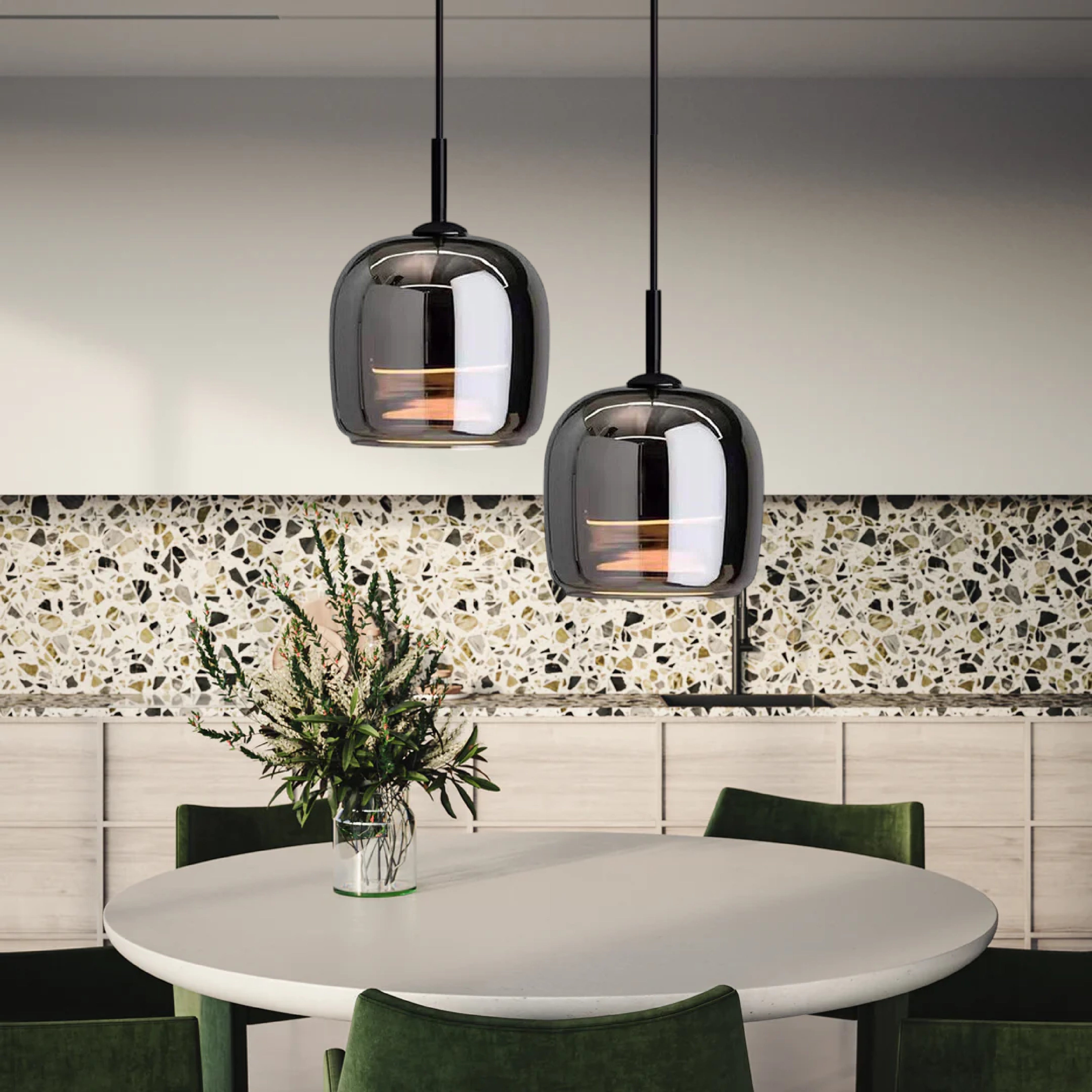 Smoked glass pendant light hanging over a modern kitchen table with minimalistic industrial design, surrounded by white and green decor elements.