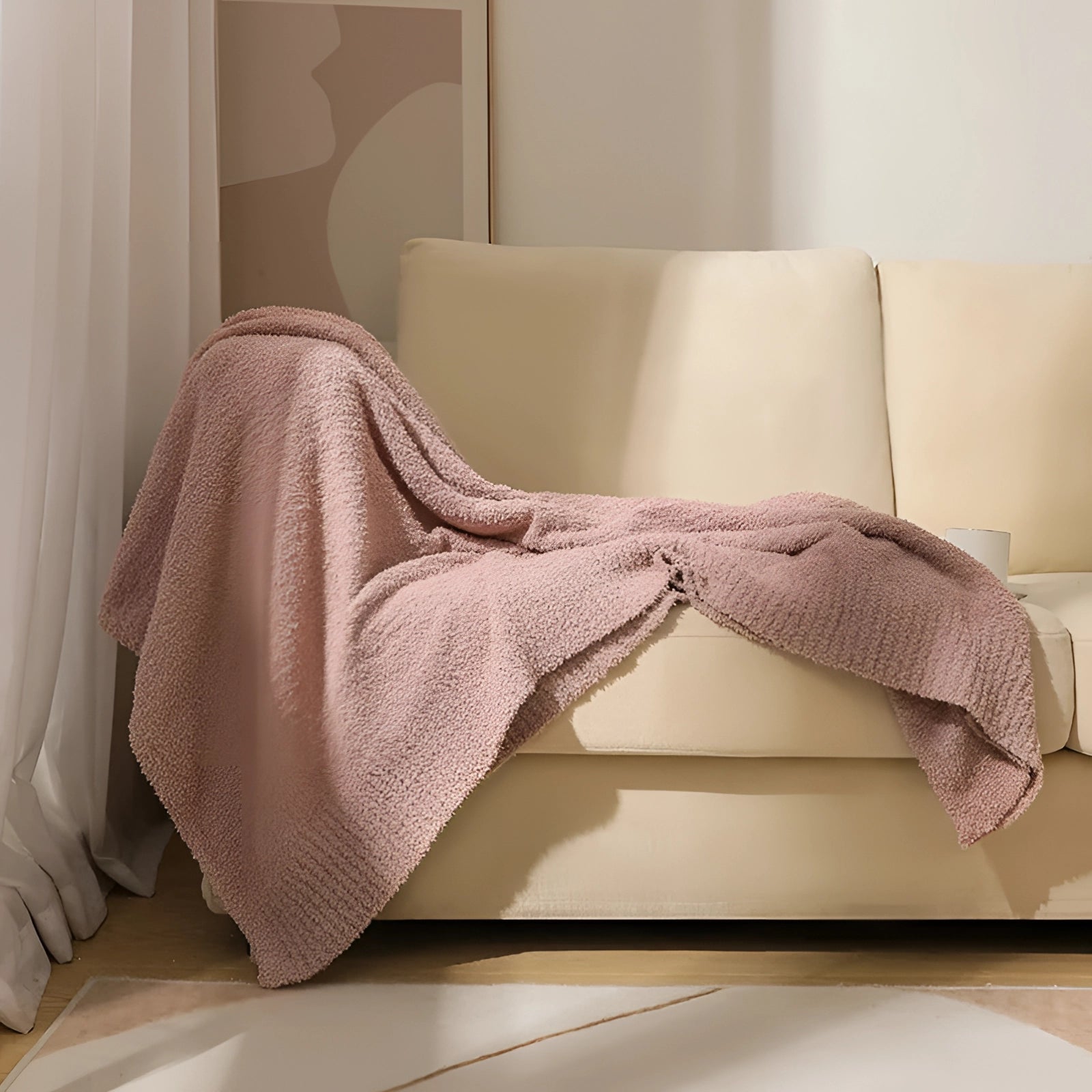 Plush pink velvet blanket draped over a beige wooden floor, showcasing its soft and cozy texture in an interior setting.