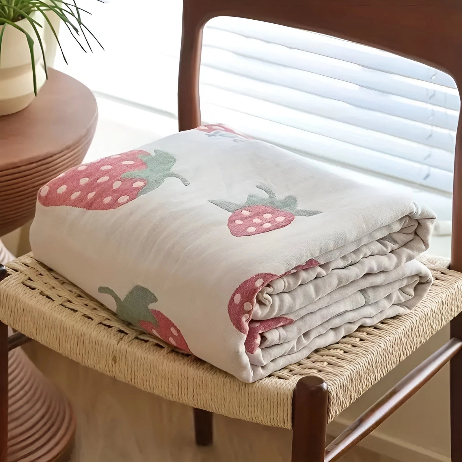 Strawberry pattern blanket draped over a couch, featuring vibrant strawberry designs on a soft textile, surrounded by comfortable bedding and decorative pillows.