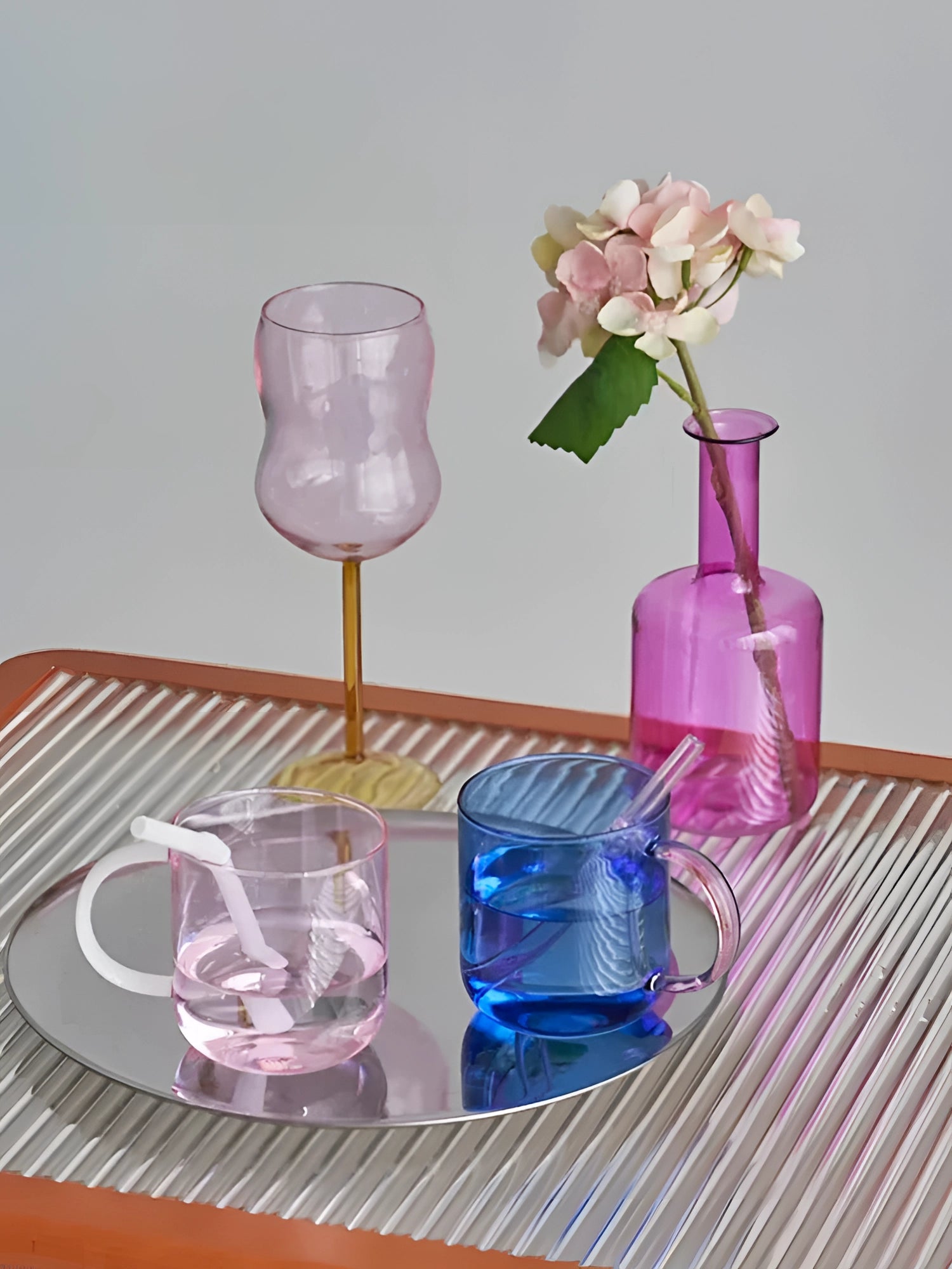 Elegant pink glass coffee and tea mug featuring a delicate floral petal design in shades of pink and purple, filled with liquid, showcasing its unique and stylish glassware appeal.