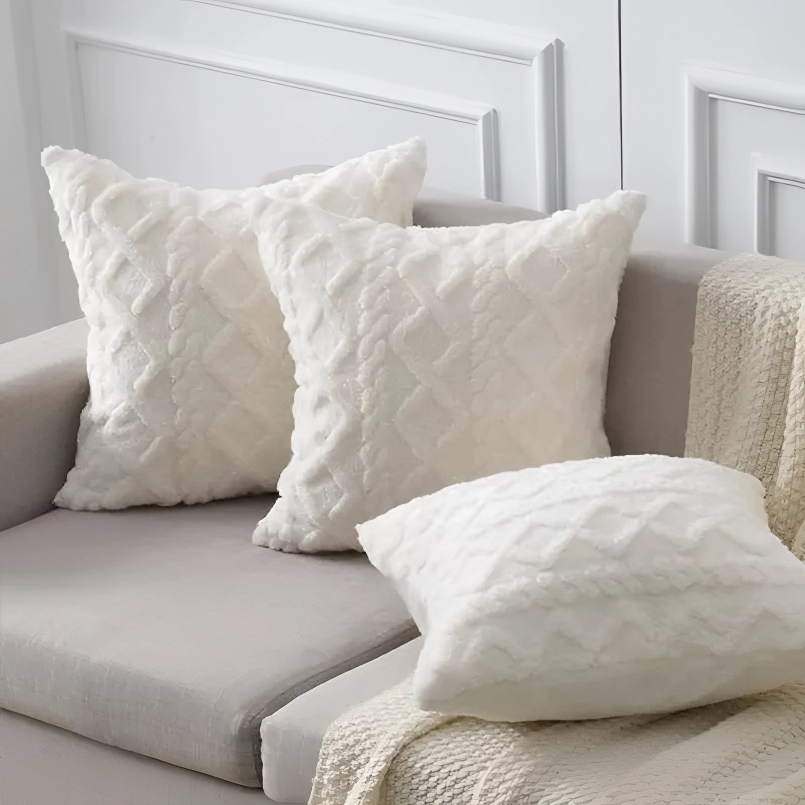 Textured velvet throw pillows in a geometric multi-color design, placed on a white and grey furniture setting, showcasing a blend of comfort and modern interior design.