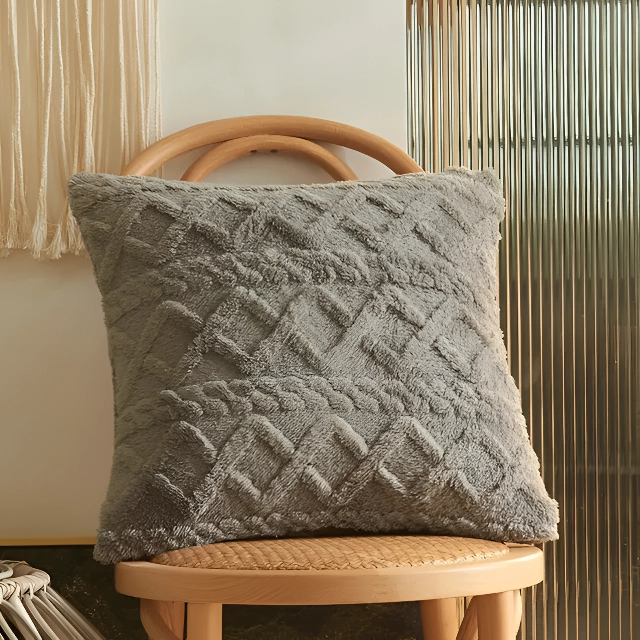 Textured velvet throw pillows in a geometric multi-color design, featuring a set of six pieces in gray, displayed on a chair with wood accents and a lightly patterned curtain in the background.