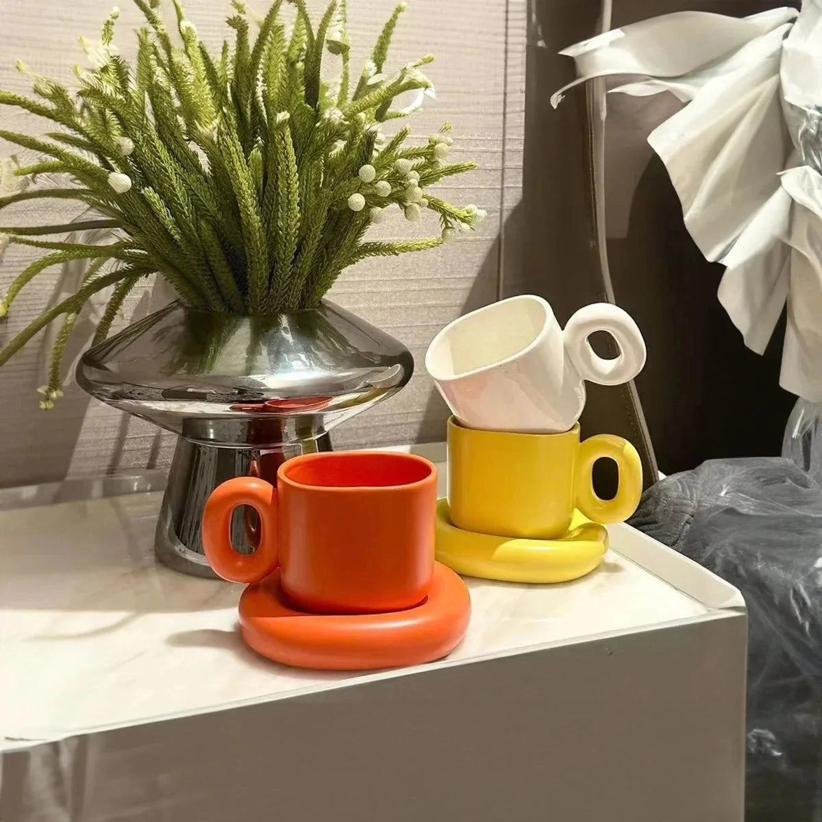 Turquoise ceramic mug with a unique handle and modern design, resting on a surface next to a small houseplant.