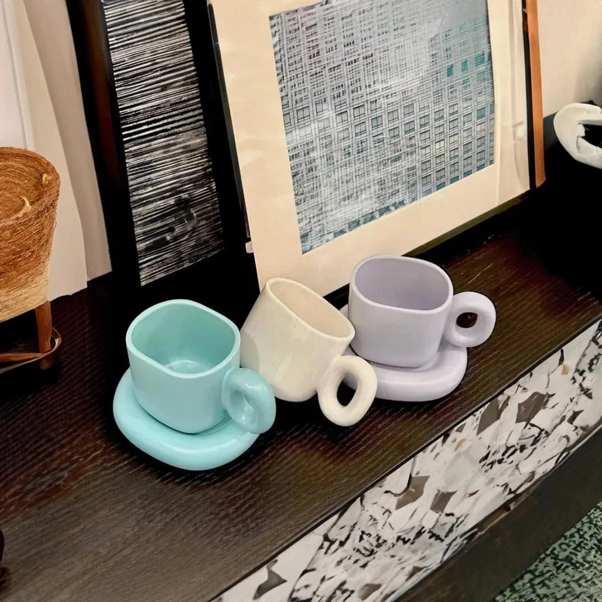 Turquoise ceramic mug with a unique handle design, placed on a wooden table. The modern designer coffee cup stands out with its vibrant color and contemporary style, surrounded by neutral tableware elements.