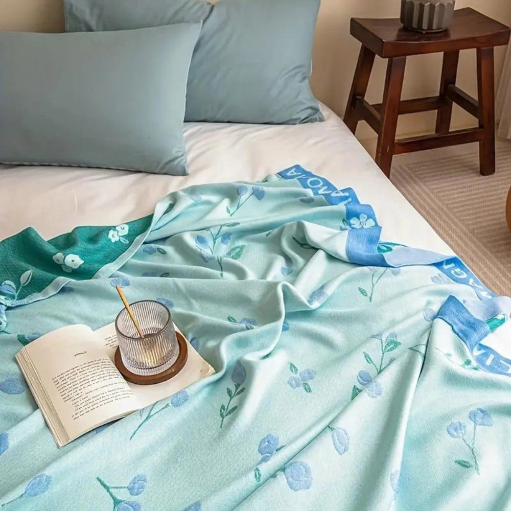 Turquoise floral designer bamboo cooling blanket in king size, draped over a bed with white linens and pillows.