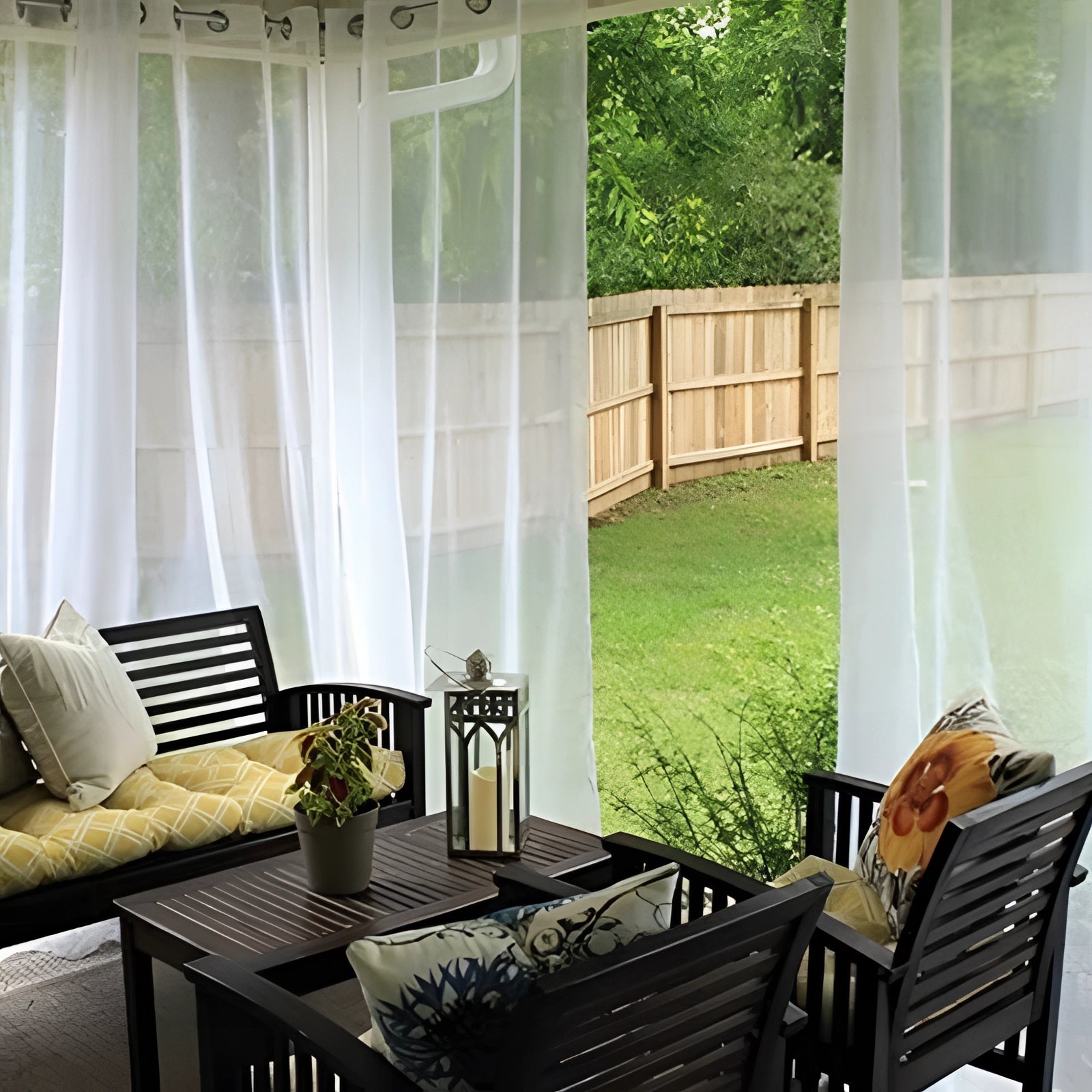 Outdoor seating area with sheer waterproof curtains, providing shade from UV rays. The scene includes a wooden table and couch, enhancing the outdoor furniture setup.